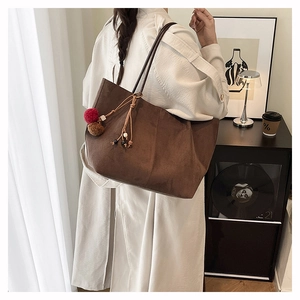 Detailed view of brown suede tote bag with fringe charm and long shoulder strap