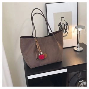 Détail du sac cabas en daim marron foncé avec pompons colorés dans un décor de maison cosy