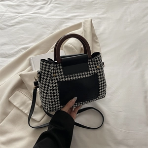 Retro houndstooth handbag with wooden handle and black leather details on a soft background