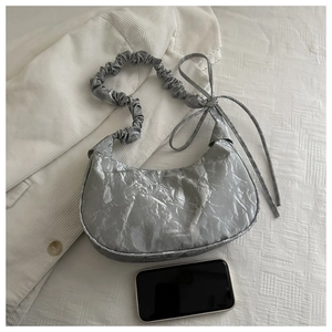 Dettaglio borsa a mezzaluna argento pieghettata con fiocco e smartphone per confronto