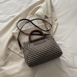 Vintage houndstooth pattern handbag with wooden handle and brown leather strap on blazer background