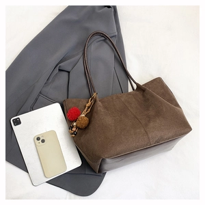 Detail of dark brown suede tote bag with decorative pendant and laptop for commute
