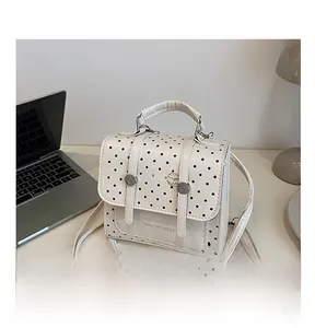 Detailed view of white polka dot PU leather bag with metal buckles on office desk