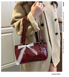 Détail d'un sac à main bordeaux brillant avec un nœud en dentelle blanche et rivets