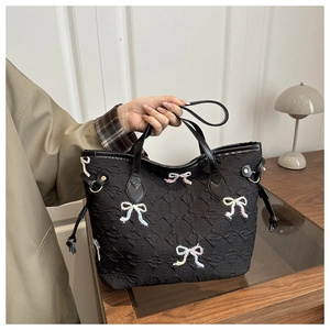 Detail of black quilted tote bag featuring colorful bow embroidery and side drawstring