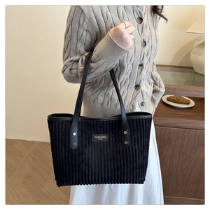 Dettaglio borsa tote in velluto a coste nero con manici in pelle e logo del marchio