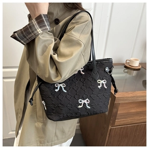 Détail du sac fourre-tout noir matelassé avec nœuds brodés sur un trench-coat kaki