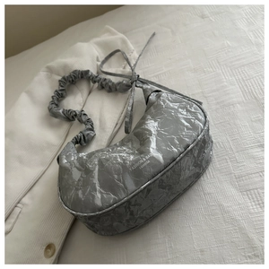 Dettaglio della borsa a spalla plissettata argento con fiocco e trama marmorea