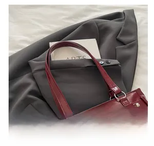 Détail du sac cabas bordeaux avec nœud en dentelle et rivets sur un blazer gris