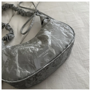 Dettaglio borsa a mezzaluna argento con texture stropicciata e tracolla arricciata soft