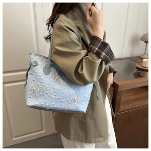 Vue détaillée du sac bleu clair matelassé avec nœuds brodés et motifs de lettres