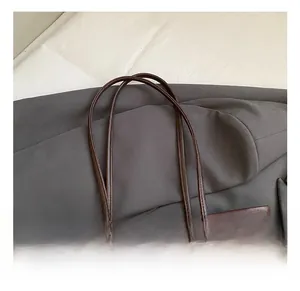 Gros plan sur l'anse du sac cabas en cuir marron grainé avec un porte-clés ours