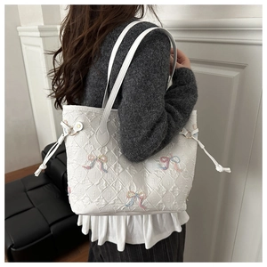 Detail of white quilted tote bag featuring colorful bow embroidery and side drawstring