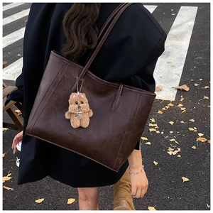 Détail d'un grand cabas marron foncé en cuir avec logo et breloque ours en peluche
