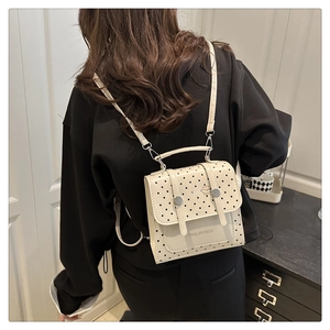 Close-up of cream polka dot backpack with silver hardware on model's back in indoor setting