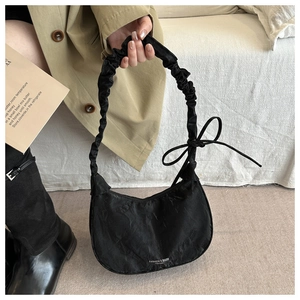 Detail of black crescent shoulder bag with pleated handle and decorative bow accent