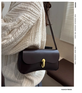 Detail of a vintage dark brown leather shoulder bag with gold oval clasp on a white knit sweater