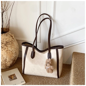 Détail du sac fourre-tout crème avec bordure brune et charm ours en peluche sur un tapis tressé