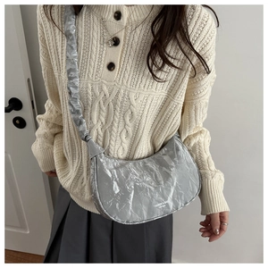 Detail of silver crinkle effect crescent bag with shoulder strap worn over knitwear