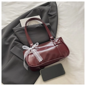 Détail du sac baguette en cuir bordeaux avec de délicats nœuds en dentelle blanche