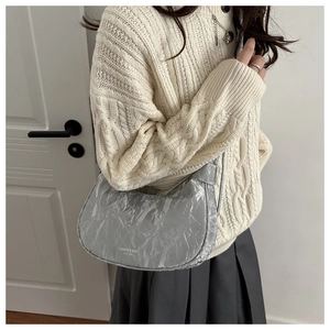 Close-up of metallic silver crescent bag with ruched texture on a knit sweater outfit