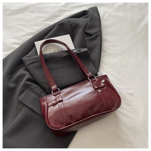 Détail du sac Boston vintage rouge foncé avec rivets argentés sur costume gris et dentelle