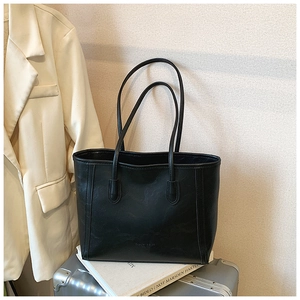 Détail d'un sac cabas en cuir noir avec fines anses posé sur une valise argentée