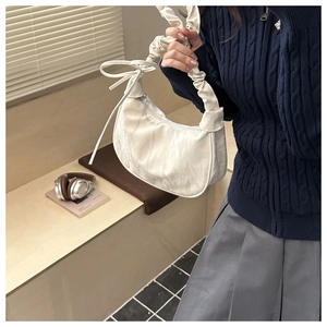 Detail of white half-moon underarm bag featuring ruched cloud handle and ribbon tie
