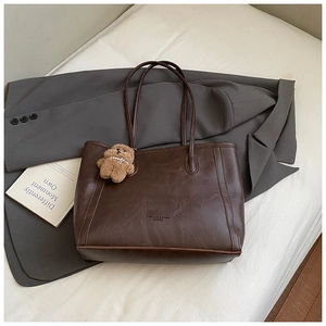 Détail d'un cabas marron foncé avec texture cuir vintage et breloque ours en peluche
