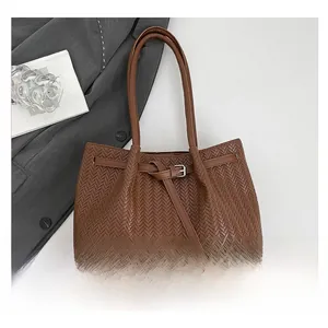 Detail of brown woven tote bag with V-pattern leather and buckle strap on white background