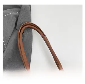 Close-up of the smooth brown leather double handles and woven texture of the tote bag