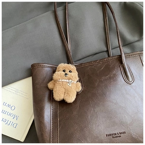 Détail d'un grand sac cabas en cuir marron foncé avec un pendentif chien en peluche