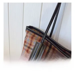 Macro detail of high-quality stitching on plaid tote bag with leather handle joinery