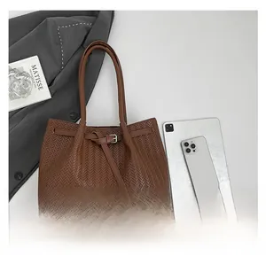 Detail of dark brown woven tote bag with leather buckle strap and business accessories