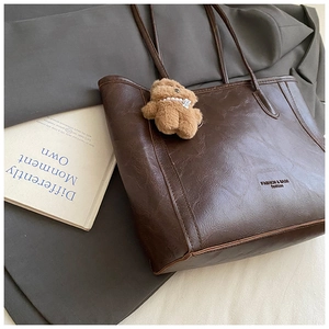 Détail d'un grand cabas marron foncé avec breloque d'ours en peluche et texte blanc