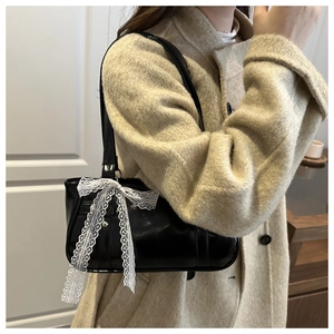 Détail du sac à bandoulière noir brillant avec nœud en dentelle blanche et boucle métal