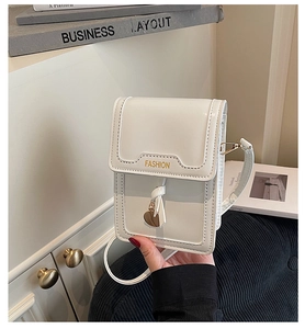 Close-up of white mini crossbody bag with gold FASHION text and heart pendant charm