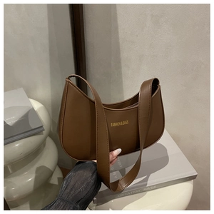 Close-up of a brown leather crescent shoulder bag styled with lifestyle accessories
