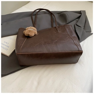 Détail d'un grand sac cabas en cuir marron foncé avec un charm ours sur fond de mode