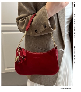 Detail of red crescent shoulder bag with cherry charm and gold chain strap on model