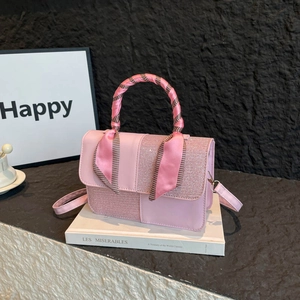 Pink crossbody bag with scarf-wrapped handle and elegant paneled texture on white books