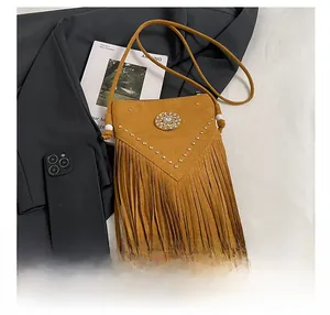 Macro detail of mustard suede crossbody bag featuring retro rivets and fringe accents