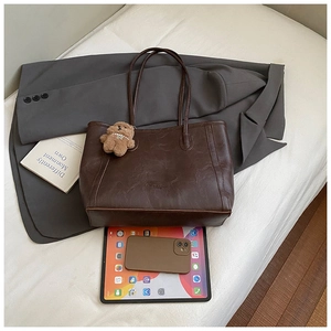 Détail d'un sac cabas en cuir marron foncé avec breloque ours et tablette en situation
