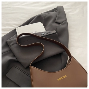 Detail of a brown crescent moon bag draped over a grey suit with fashion lettering
