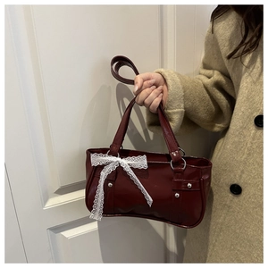 Détail d'un sac à main bordeaux brillant avec nœud en dentelle blanche et anneau