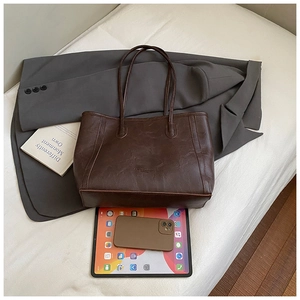 Gros plan d'un grand sac cabas marron foncé montrant sa capacité avec tablette et portable