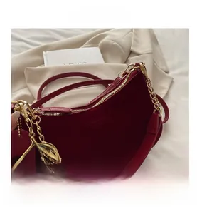 Detail of dark red suede moon bag featuring gold chain and cherry charm accessory