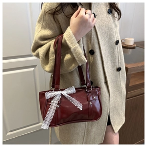 Detail of dark red bag featuring a large white lace bow and glossy synthetic leather finish