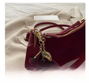 Detail of red faux suede handbag featuring gold zipper and cherry metal charm pendant
