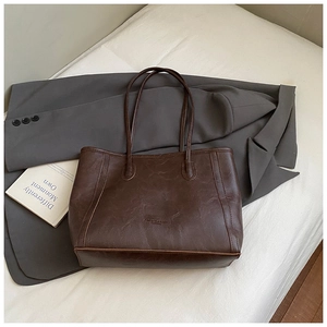 Détail d'un grand cabas marron rétro plissé posé sur un blazer gris et un lit blanc